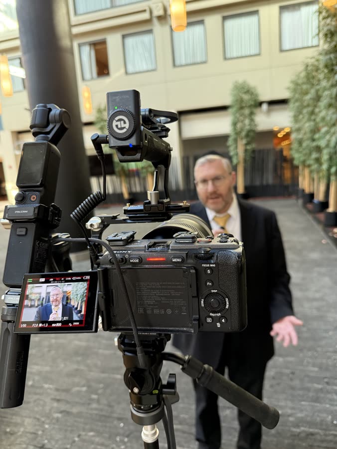 The camera on a tripod filming a man in a suit gesturing