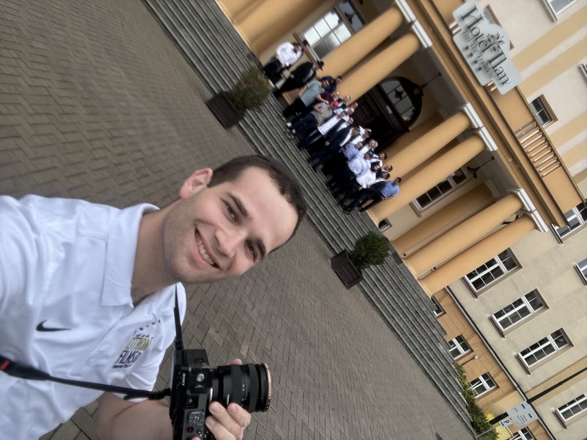 Yaakov smiling with the camera in hand, a group of young men lined up behind him for a shot