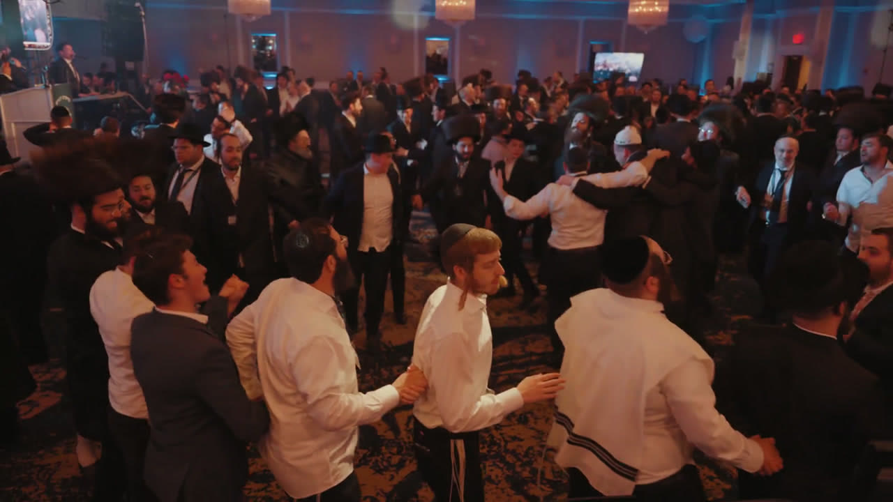 A packed ballroom of men dancing in circles under blue light at an MDY event