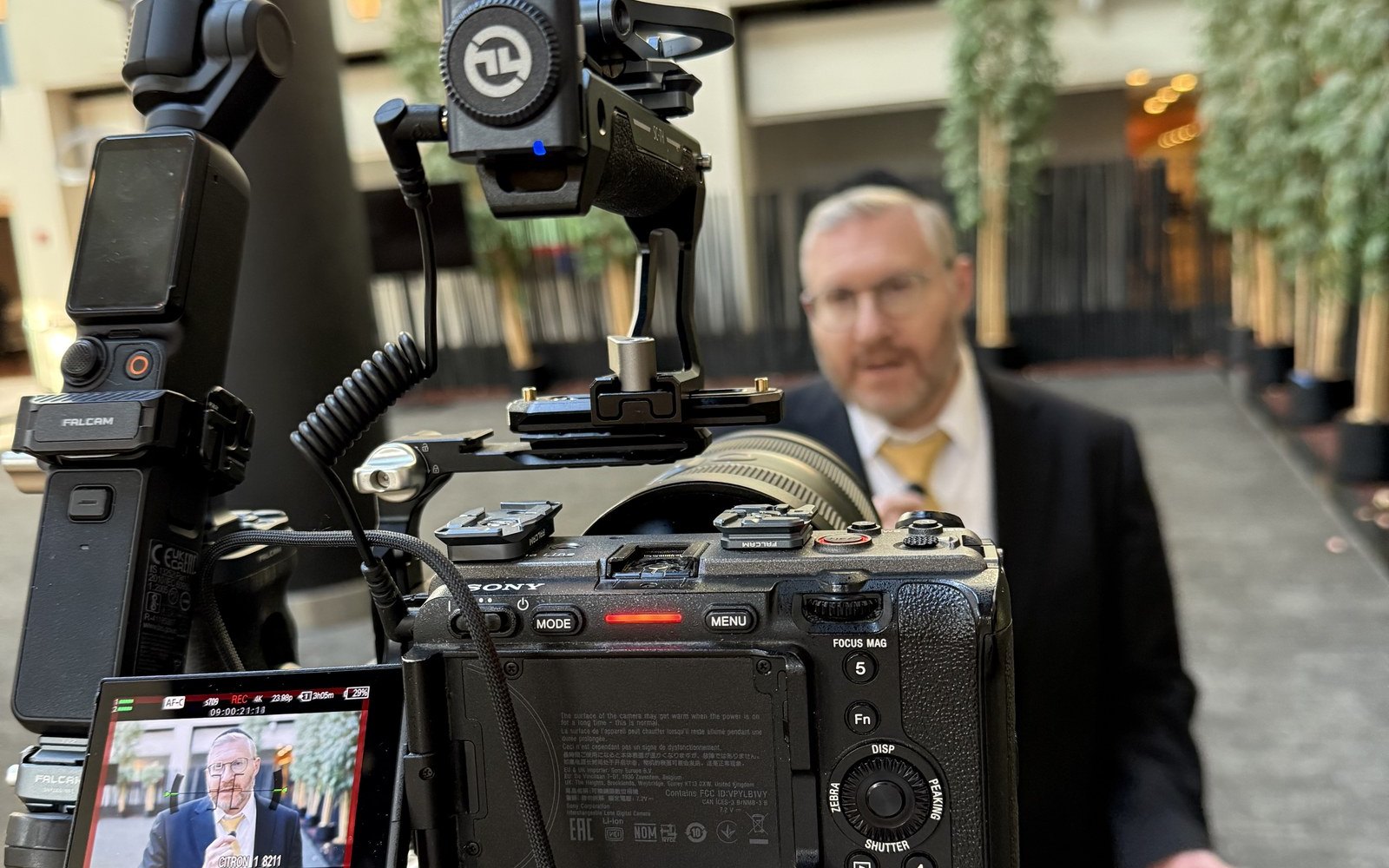 Our camera on its tripod in the hotel atrium, a guest in a suit answering it, his face on the camera's screen